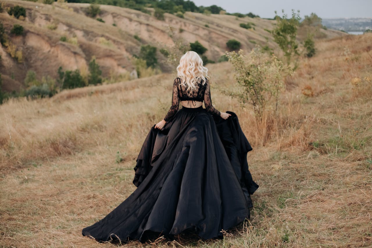 creative-02 Back view of a woman in a black dress walking through a picturesque rural landscape.