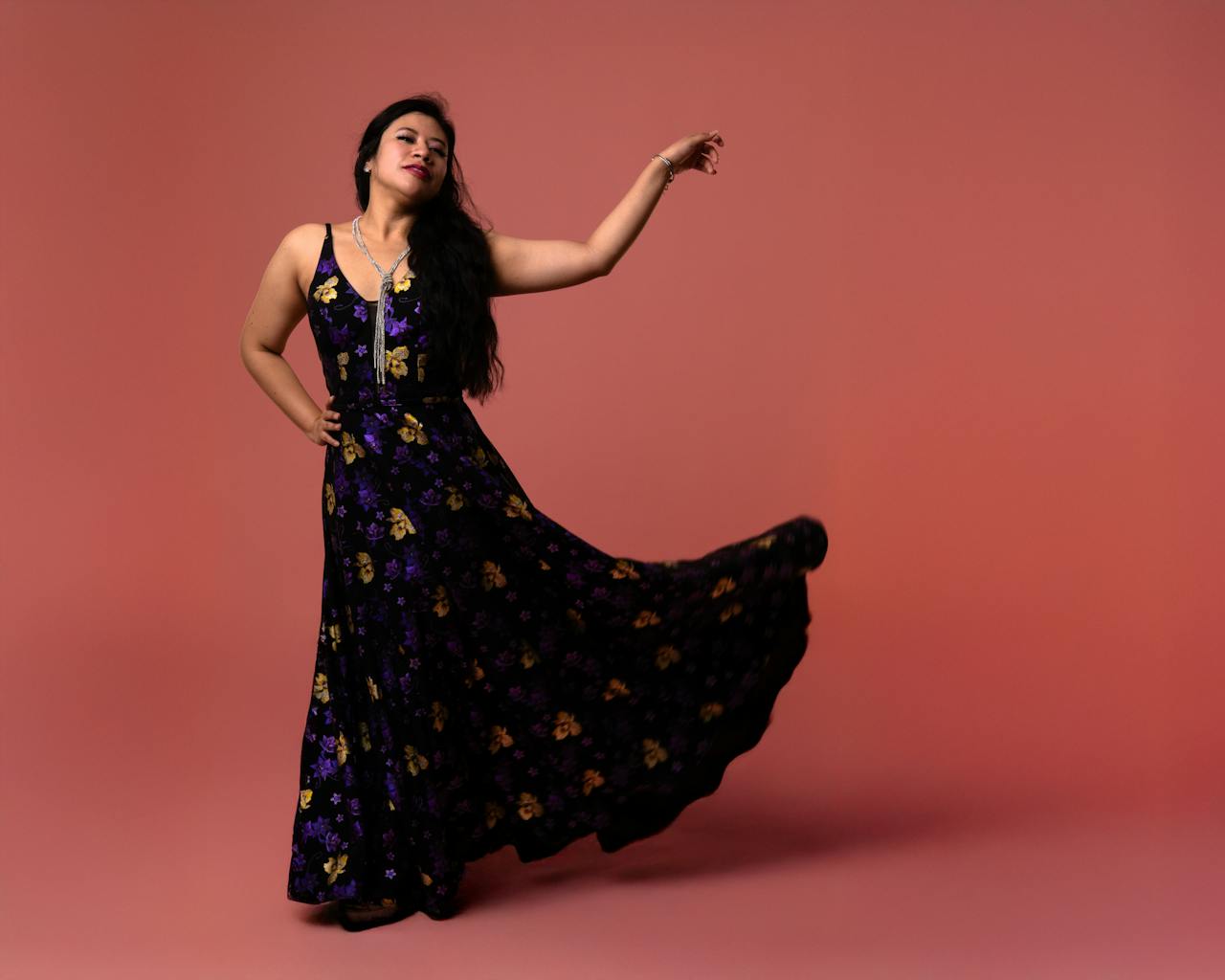 creative-02 Portrait of a woman in a floral maxi dress posing gracefully against a pink background.