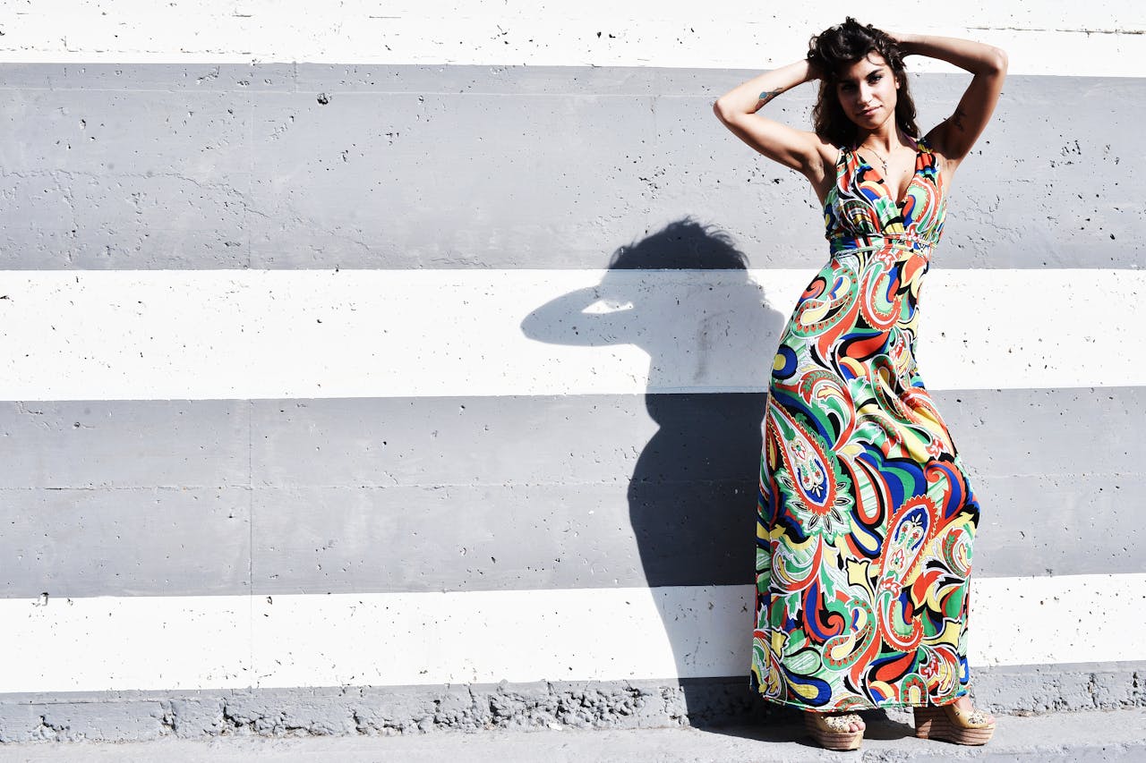 digital-01 Stylish woman posing in colorful dress against a striped wall under bright daylight.